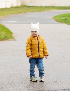 Sonbahar parkında yürüyen sarı ceketli şirin çocuk.