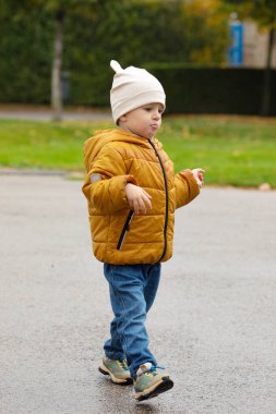 Sonbahar parkında yürüyen sarı ceketli şirin çocuk.
