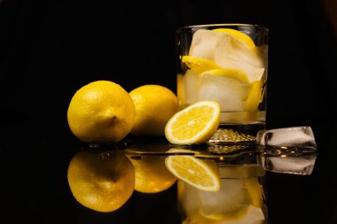 Siyah yansıyan yüzeydeki bir bardakta limon ve buz.