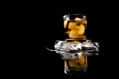 Bir bardak buzlu içecek. Önünde buz küpleri var. Yansımalı buza odaklı.