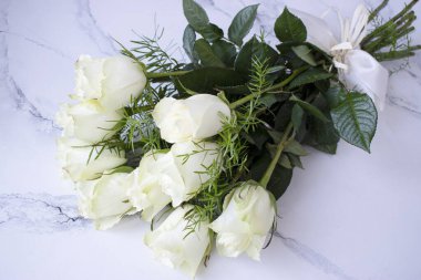 Bir demet beyaz gül, beyaz bir taş masanın üzerinde.