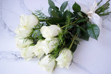 Bir demet beyaz gül, beyaz bir taş masanın üzerinde.