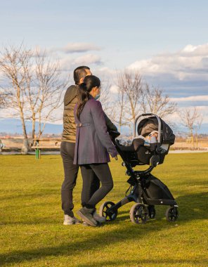 Asyalı bir çift, bebekleriyle parkta at arabasında yürüyor. Sokak manzarası, seyahat fotoğrafı, seçici odaklanma. Beyaz Kaya, BC, Kanada-8 Nisan 2021