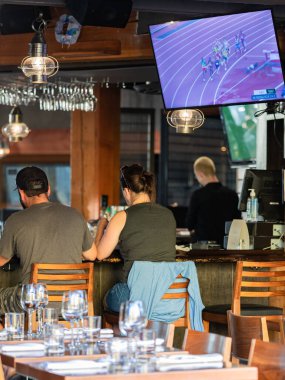 29 Temmuz 2021-Vancouver BC, Kanada 'da büyük ekran TV' de bir çiftin bir barda dinlenip maç izlediği arka manzara. Sokak görüntüsü, seçici odak.