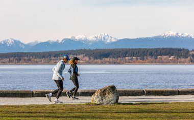 Aktif kıdemli çift parkta koşuyor ve koşuyor. Sokak görüntüsü, seçici odak, metin için kopyalama alanı 8 Mart 2021-Beyaz Kaya, BC, Kanada