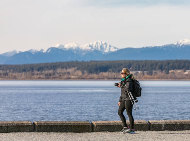 Fotoğrafçı kadın, el ele tutuşan kameraman gezgin parkta yürüyor. Sokak görüntüsü, seyahat fotoğrafı, metin için kopya alanı 8 Mart 2021-White Rock BC, Kanada