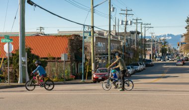 Sokakta bisiklet süren bir aile. Baba ve çocuklar bisikletle karşıdan karşıya geçiyorlar. Babası çocuklarını 18 Nisan 20.2021-Richmond MÖ. Kanada 'ya bisiklet sürmeye götürüyor. Sokak manzarası, seyahat fotoğrafı, seçici odak