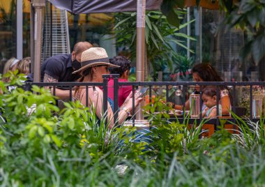 İnsanlar yaz kafesinde, şehir dışında yemek yiyor. Kadın açık hava restoranında oturuyor ve akıllı telefonunu kullanıyor. 15 Ağustos 20.2021-Vancouver BC, Kanada. Sokak görünümü, seçici odak, bulanık arkaplan.