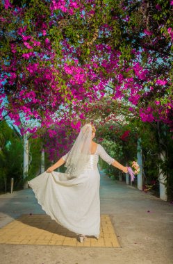 Çiçek bahçesinde güzel bir gelin. Gelinlik giymiş güzel, zarif bir kadın. Bahçede pembe çiçeklerle tek başına dolaşıyor. Seçici odak, bulanık.