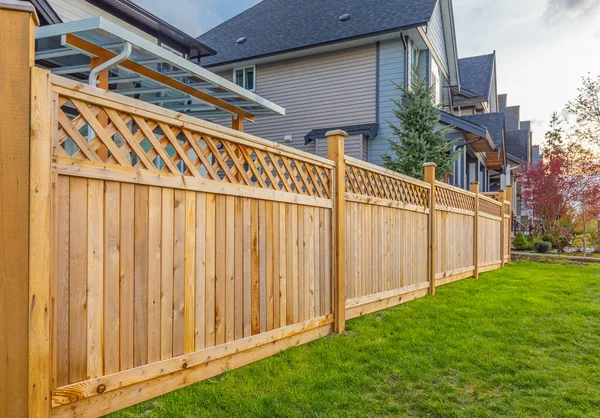 Pěkný dřevěný plot kolem domu. Dřevěný plot se zeleným trávníkem a stromy. — Stock fotografie