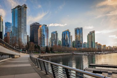 Vancouver 'daki Harbor' ın çarpıcı manzarasında şehir merkezindeki güzel binalar, gün batımında tekneler. Vancouver BC, Kanada Limanı, Gezinti güvertesinde yürüyen turistler - 11 Nisan 2022 - Seyahat fotoğrafı
