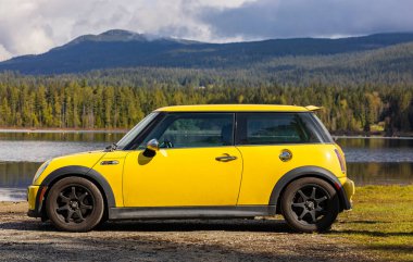 Sarı Mini Cooper S arabasının yan görüntüsü doğal arka planda. Sarı Mini Cooper park yeri 27 Nisan 2022-Whonnock Gölü BC, Kanada-Seyahat fotoğrafı, kimse, seçici odak