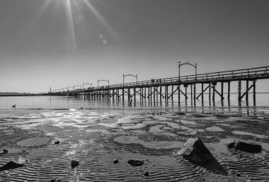 Beyaz Kaya 'daki ahşap iskele, BC çapraz olarak görüntüye yayılıyor. Parıldayan ışıklar denize yansıyor. Siyah ve beyaz görüntü: Gün batımında sahil ve iskele, Surrey, BC, Kanada-22 Şubat 2022