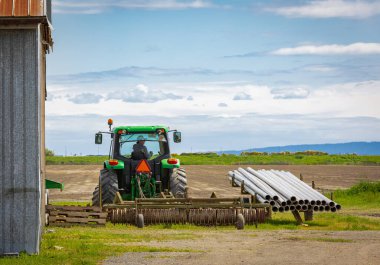 Traktördeki çiftçi tarlaları hazırlıyor. Tarım traktörü tarlaları sürüyor, tarlaları ekime hazırlıyor. Seçici odak - 29 Mayıs 2022-Delta BC, Kanada