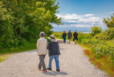 Güneşli bir günde bahar parkında yürüyen insanlar. Sıcak, güneşli bahar günü. Doğada vakit geçirmek. Huzurlu bir atmosfer. Arka plan, seçici odak, seyahat fotoğrafı - 29 Mayıs 2022-Delta BC Kanada