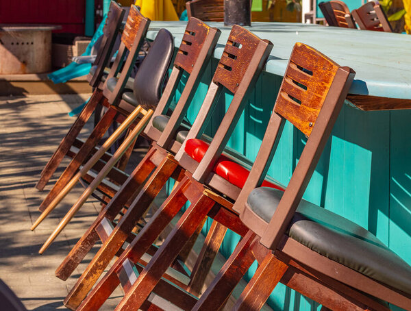 Tall wooden bar stools with backs stand in a row near the bar counter. Row of a tall chairs at the counter with beautiful natural sunlight. Outdoor furniture. Close up. Selective focus.