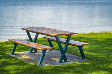 Kanada 'nın Okanagan Gölü' ndeki bir yaz parkında sandalyeli boş bir tahta masa. Göl kenarında güneşli sıcak bir gün. Gündoğumu manzarası. Seyahat fotoğrafı, hiç kimse, metin için alanı kopyala