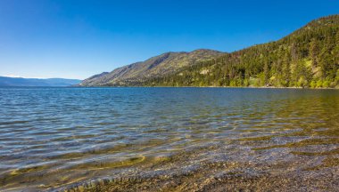 Okanagan Gölü Kanada. Yaz manzaralı bir göl ve sabahın erken saatlerinde arka planda dağlar. Rahatlamayı kabul et. Turistler ve doğa yürüyüşleri için mükemmel bir yer. Seyahat fotoğrafı, hiç kimse, kopyalama alanı