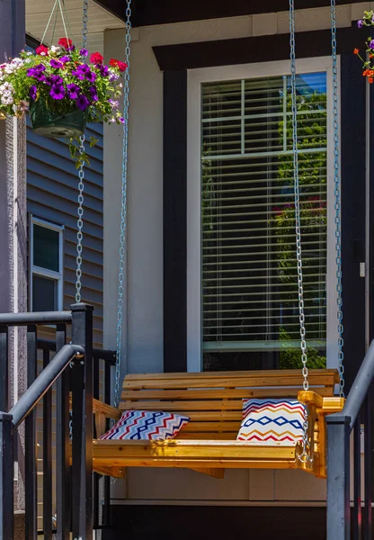 Beautiful wooden front porch swing with comfortable pillows. Outdoor wooden porch swing bench with color pillows. Nobody, street photo, selective focus