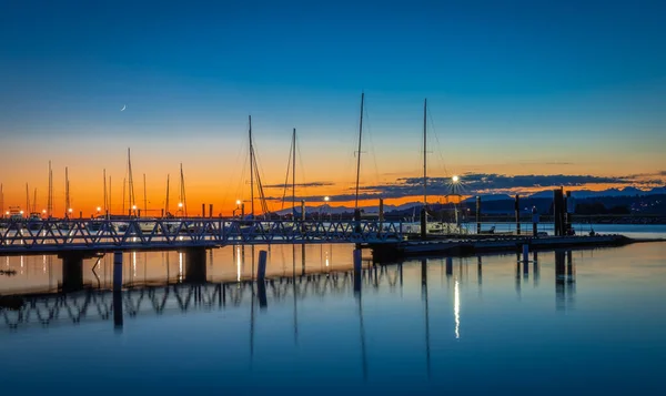 Beautiful sundown at the yacht harbor with pier. Summer sunset at the sea. Leisure time, active life, vacation and holidays concept. Marina with yachts under dark blue sky at sunset