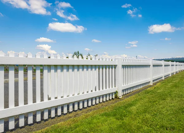 White wooden fence on the blue sky background. Green lawn and wooden white fence on sunny summer day. Nobody, copy space for text, selective focus