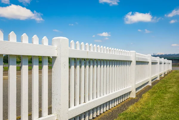 White wooden fence on the blue sky background. Green lawn and wooden white fence on sunny summer day. Nobody, copy space for text, selective focus