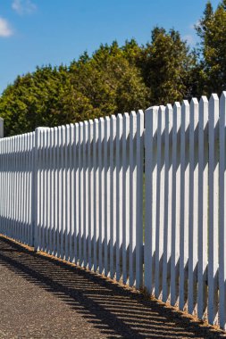 Mavi gökyüzü arka planında beyaz ahşap çit. Güneşli yaz gününde yeşil çimenler ve tahta beyaz çitler. Hiç kimse, metin için boşluk kopyala, seçici odak