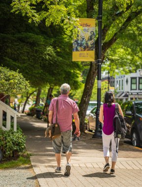 Çift güneşli bir yaz gününde şehirde yürüyüşe çıktı. Şehir caddesinde yürüyen insanlar. Sokak fotoğrafı, MÖ Langley editoryal-Kanada-5 Temmuz 2022