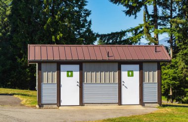Public toilet in park at sunny summer day. Wooden restroom or toilet building in remote forest in British Columbia. Bathrooms or WC. Public automatic toilets in town. Nobody