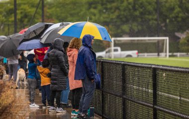 Back view of people with umbrellas standing under rain at the stadium waching football. Heavy rain, people under umbrellas. Travel photo, street view-September 4,2022-Surrey BC, Canada