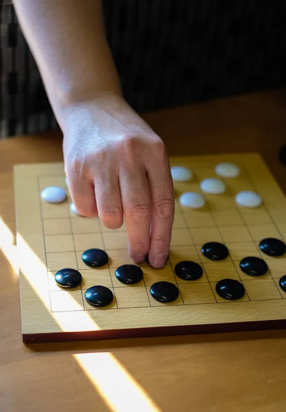 Chinese go game board, close up view of playing black and white stone pieces, Alphago. Hands of woman playing Asian board game. Selective focus