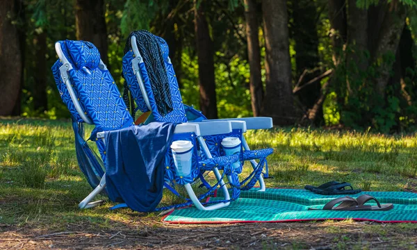 Two empty folding chair on the green grass on a sunny day. Two chairs for a picnic in the summer park. Nobody, travel photo.