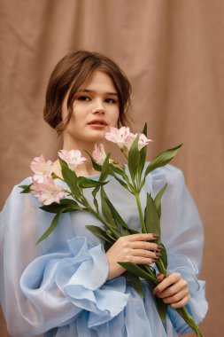 Elinde çiçekler olan mavi elbiseli bir kız.