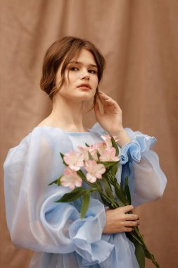 Elinde çiçekler olan mavi elbiseli bir kız.