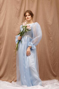 Elinde çiçekler olan mavi elbiseli bir kız.