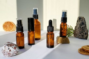  Taşlar ve turuncu, sert gölgeler içeren açık bir zemin üzerinde koyu camdan yapılmış spa kozmetik şişeleri grubu