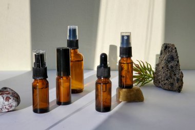  Taşlar ve turuncu, sert gölgeler içeren açık bir zemin üzerinde koyu camdan yapılmış spa kozmetik şişeleri grubu