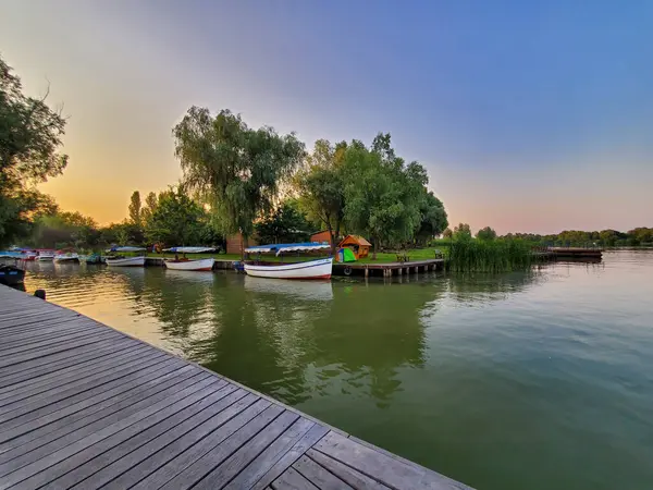 Kilátás a tóra naplementekor a mólóról, kis hajók, fák, gyönyörű táj — Stock Fotó