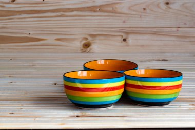 Ahşap zemin üzerinde kırmızı, mavi, sarı, turuncu ve yeşil renkte üç çizgili kâsenin fotoğrafı.