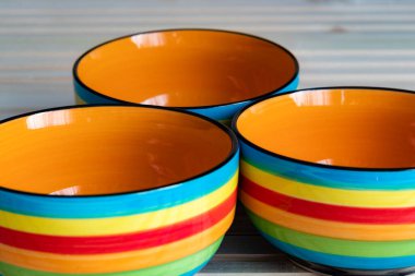 Ahşap zemin üzerinde kırmızı, mavi, sarı, turuncu ve yeşil renkte üç çizgili kâsenin yakın plan fotoğrafı.