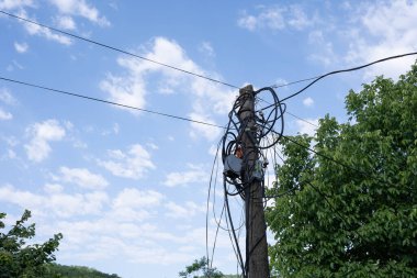 Elektrik direği, bazı elektrik dağıtım kutuları ve yazları mavi gökyüzü arka planına dolanmış gibi görünen bir sürü kablo.