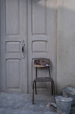 Eski ahşap kapılı eski bir binanın ön cephesi eski bir ahşap sandalye ve önünde bir kova.