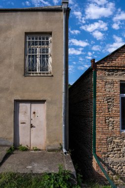 Binalar ve bina arasında küçük boş bir alan olan küçük bir kasabadaki eski bir taş binanın üzerinde penceresi olan bir kapı var, ama binanın üstünde birçok mavi gökyüzü var.