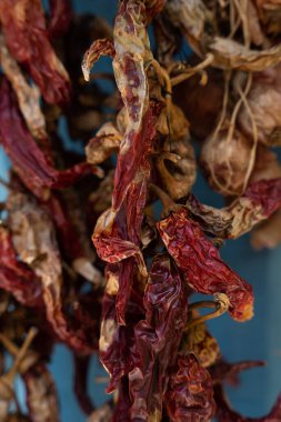 Mavi duvarda güneşte kuruyan koyu kırmızı biber asılı.