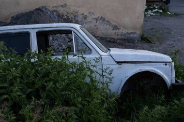 Eski beyaz Rus arabaları Niva, holde duruyordu. Arkasında bir sürü eski çöp konteynırı vardı..