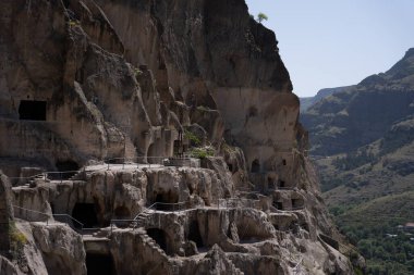 Gürcistan dağlarındaki manastırda dağ boyunca mağaralar ve geçitler var. Üzerlerinde mavi bir gökyüzü var.