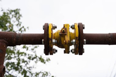 Ortasında sarı bir bağlantı olan paslı büyük bir su borusu açık mavi gökyüzüne karşı.