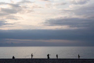 Ufukta balıkçıların karanlık siluetleriyle denizde inanılmaz romantik bir gün batımı.