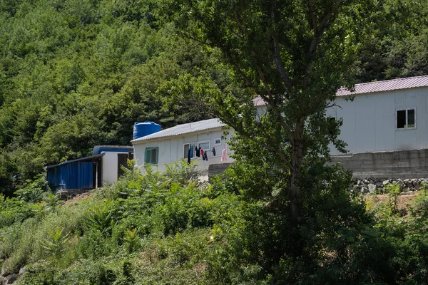 緑の茂みと木に囲まれた山の中に白いカントリーハウスがあります家には青い水の樽があり糸にリネンがかかっています — ストック写真