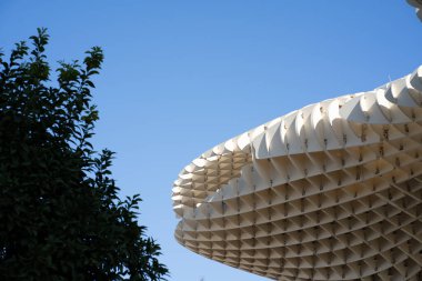 İlginç bir bina dizaynı farklı bir desen oluşturuyor ve arka plan mavi bir gökyüzü, ama karşı tarafta koyu ağaçlar var.